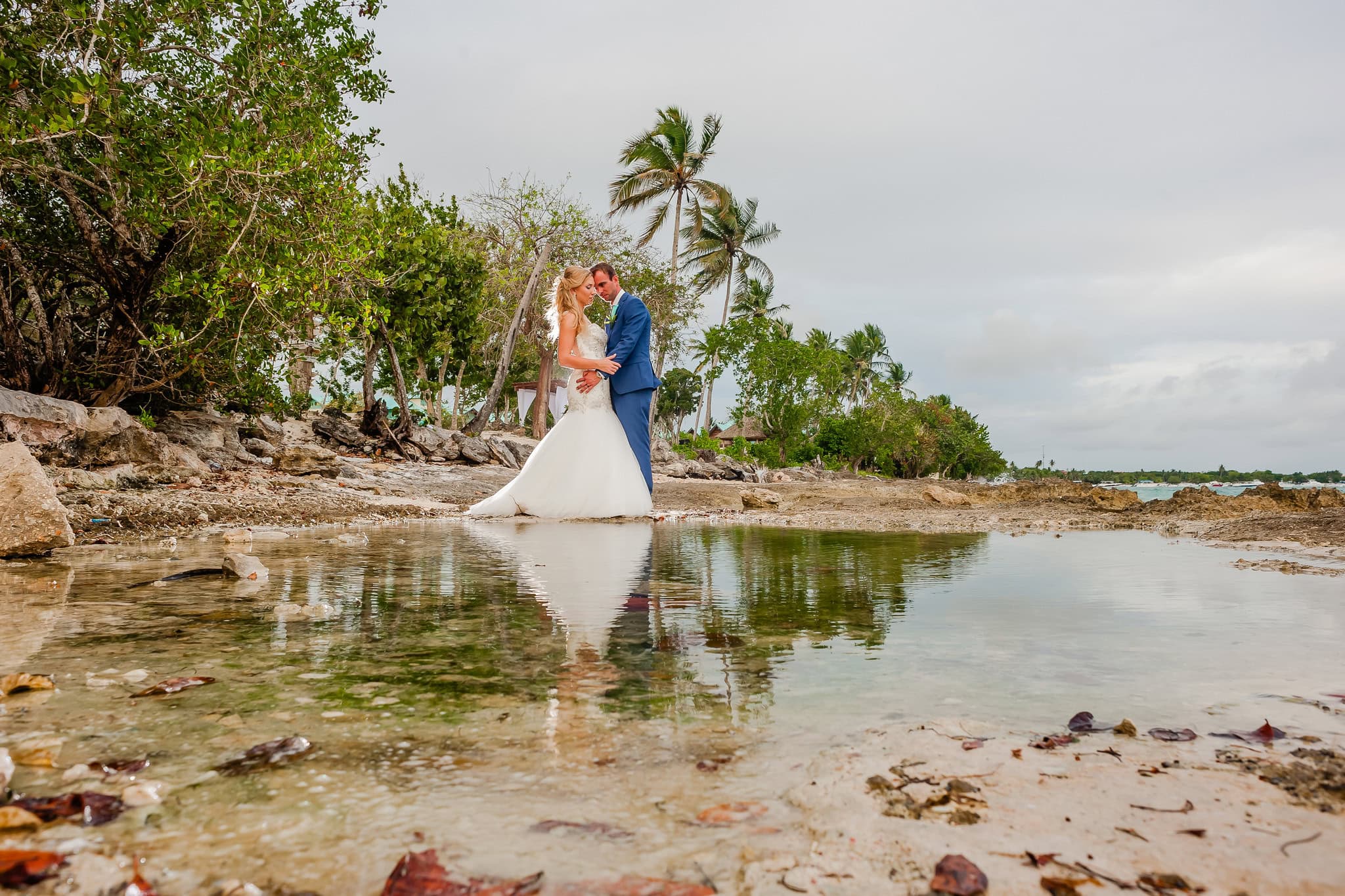 Bride and groom reflected in a tidal pool among the rocks and palms on the La Romana coast, Dominican Republic