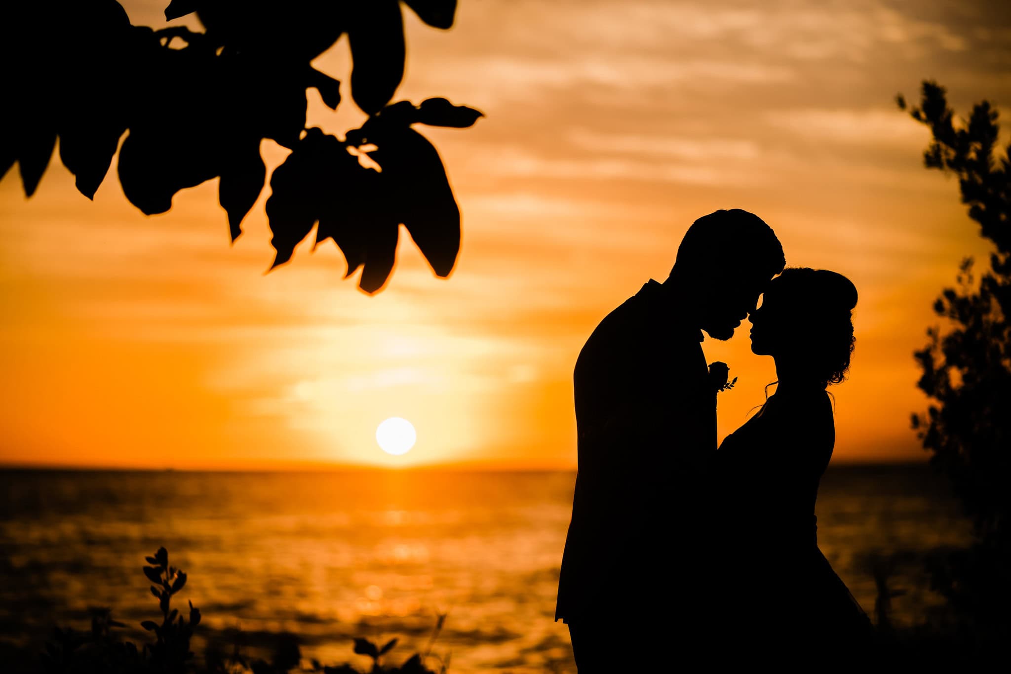 Bride and groom silhouetted forehead to forehead against an orange sunset over the sea in La Romana, Dominican Republic