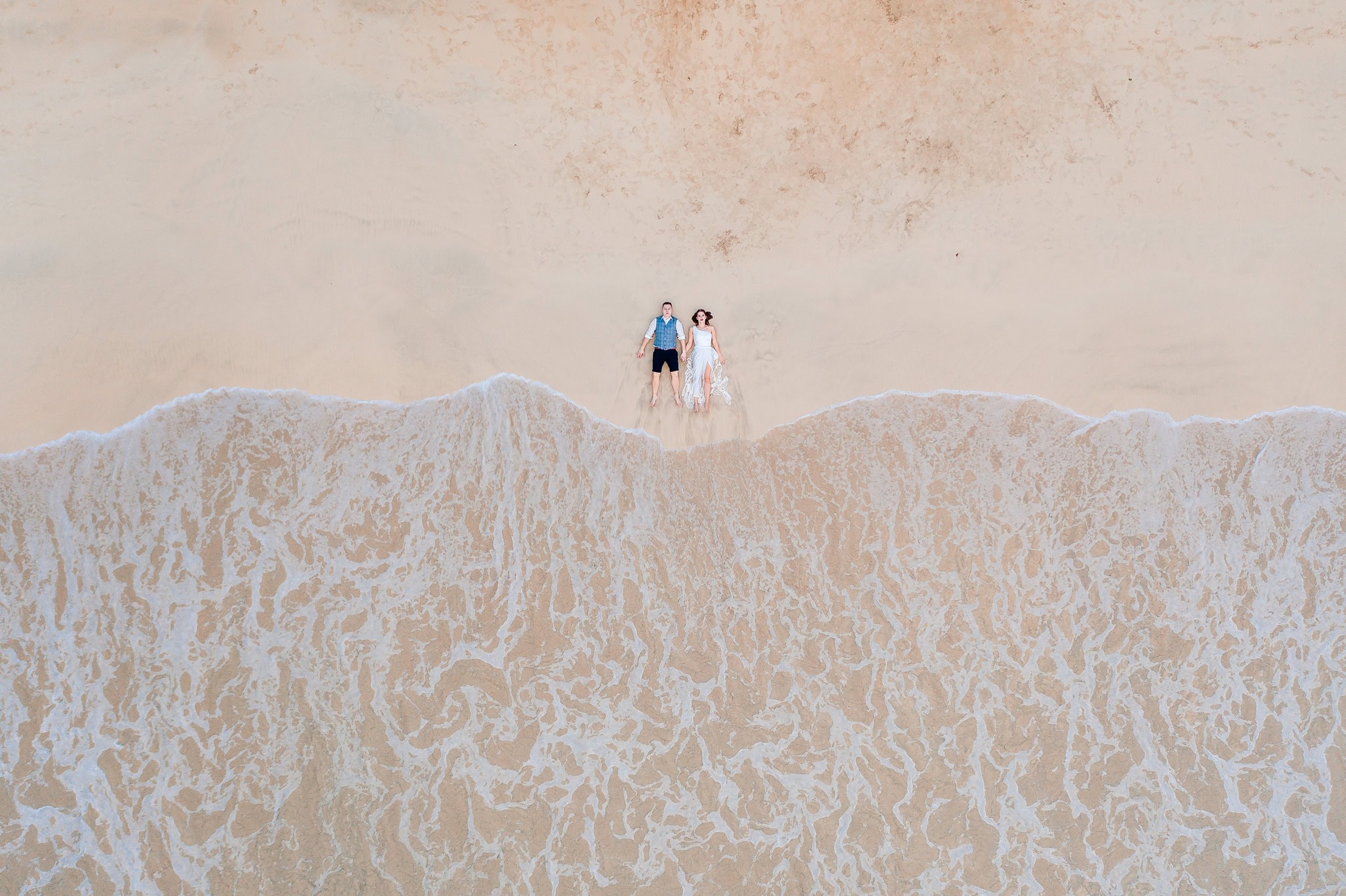 Aerial view of a couple standing on the wet sand as the surf reaches them on a beach in Las Terrenas, Dominican Republic