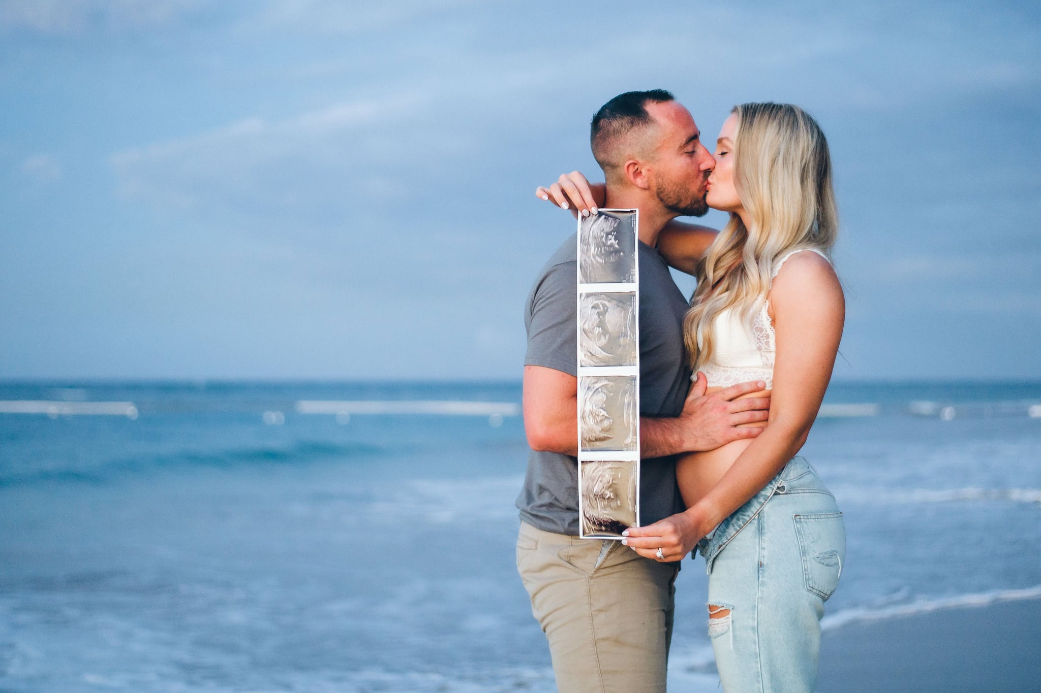 Expecting couple kissing while holding their ultrasound photos on the beach in Punta Cana