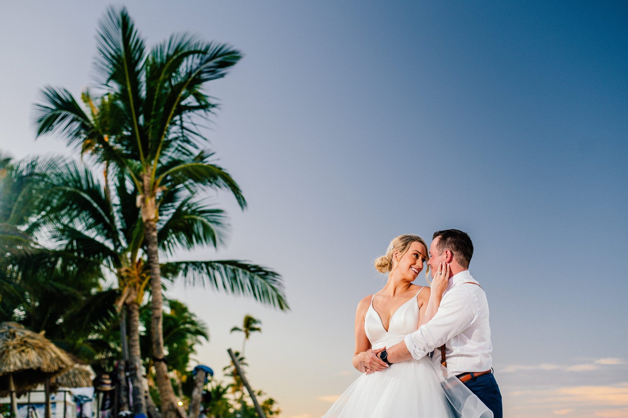 Newlyweds embracing beneath palm trees during an outdoor wedding portrait