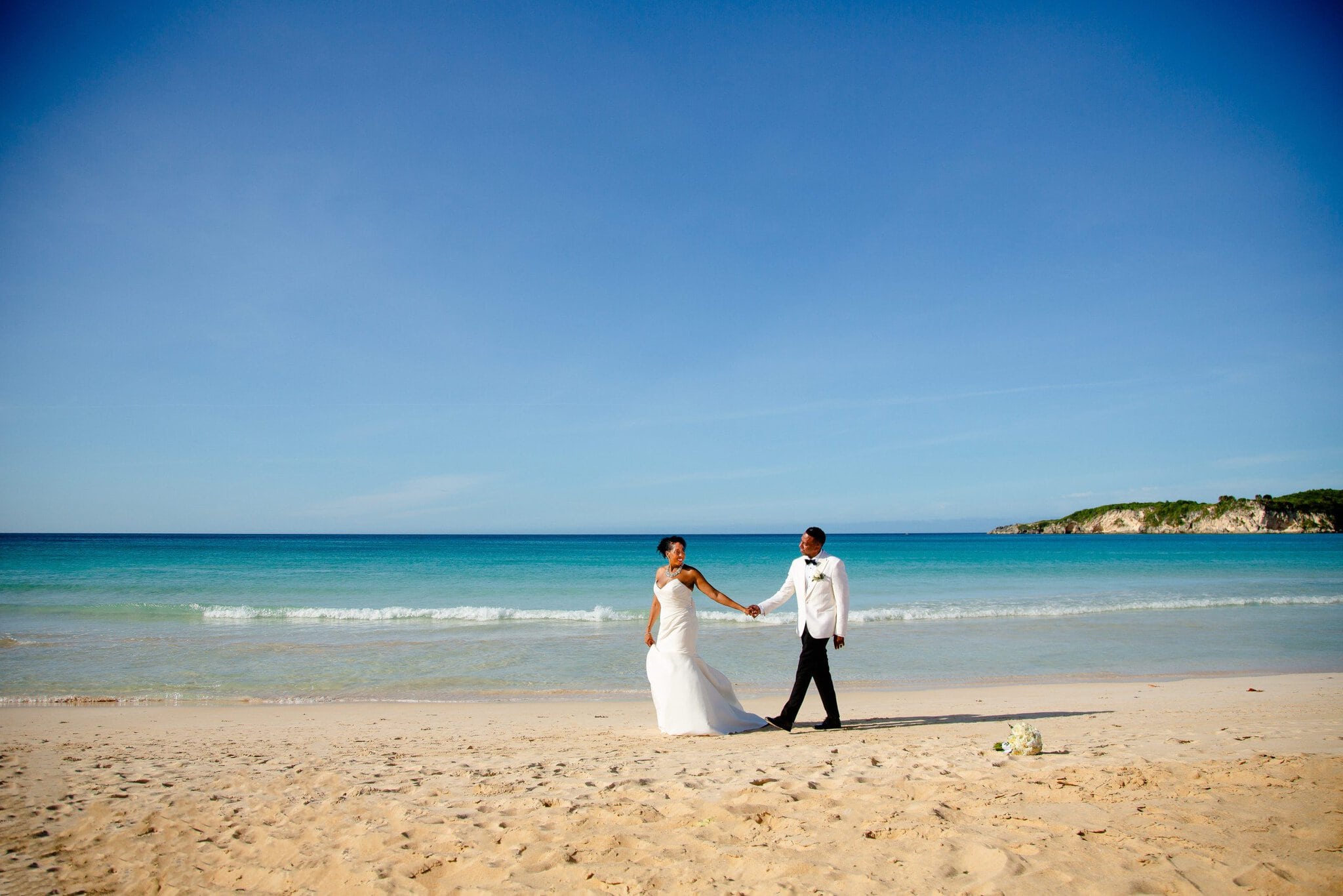 Bride and groom holding hands while walking along the beach after their wedding