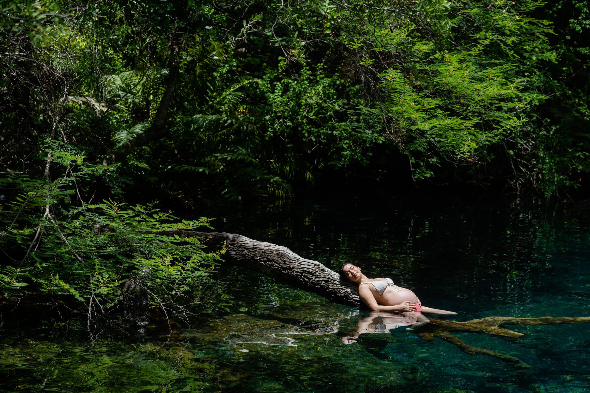 Pregnant woman reclining in the clear freshwater lagoon surrounded by dense tropical vegetation at Ojos Indígenas in Punta Cana