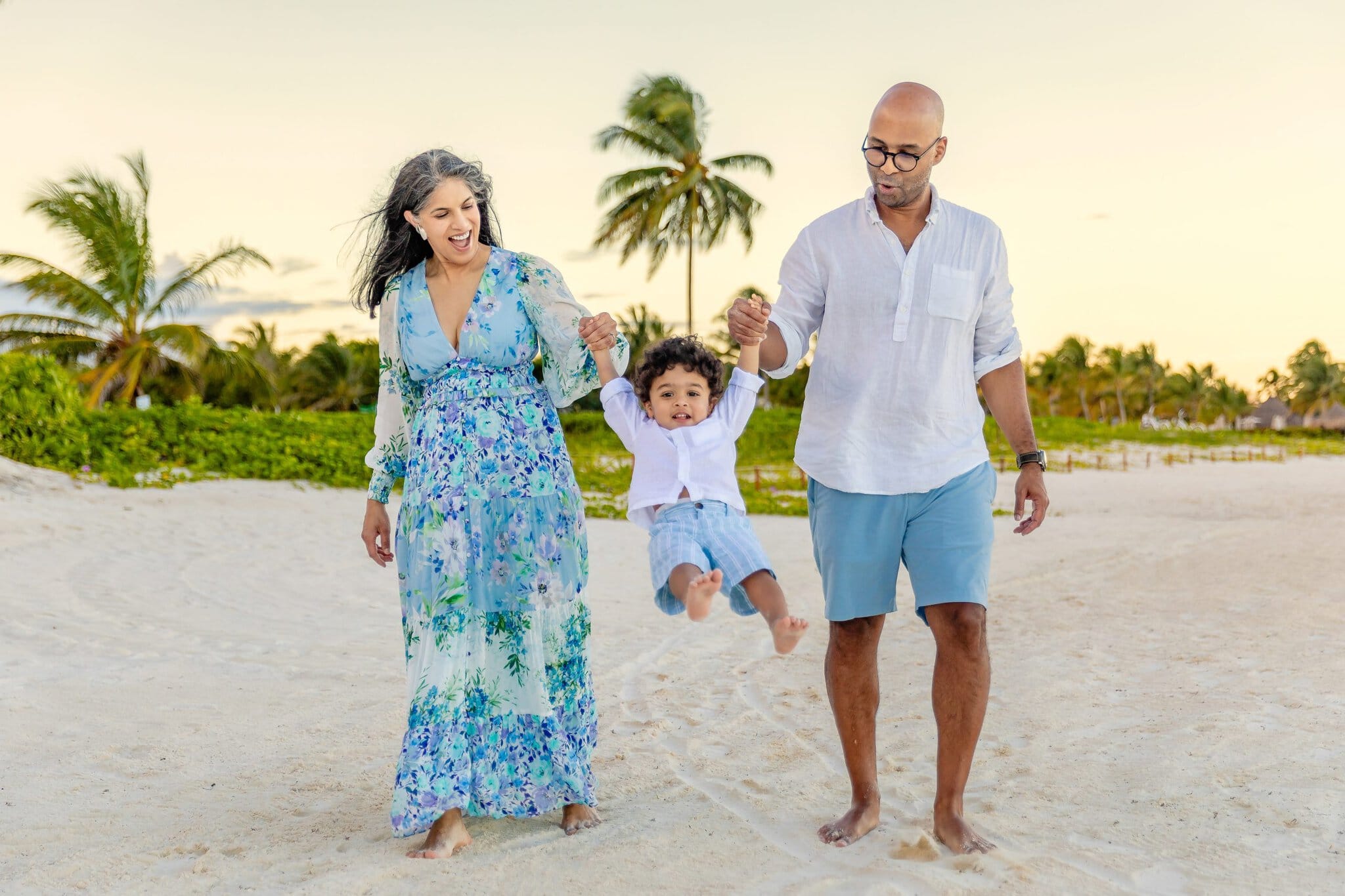 Parents holding their toddler’s hands and swinging him playfully during a family beach photo session