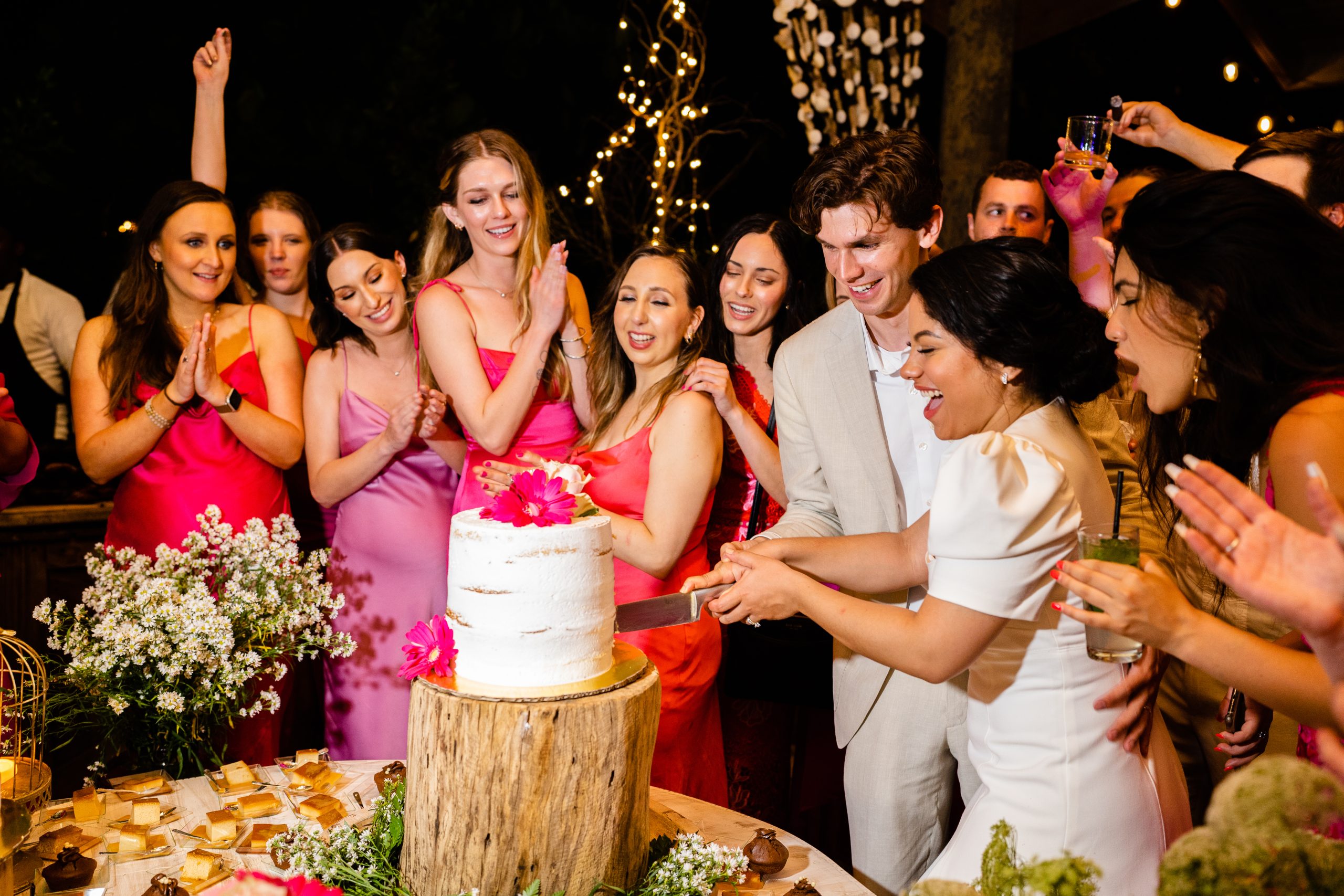 Bride and groom cutting a white cake decorated with bright pink flowers as their guests gather around at Porto by Mosquito in Las Terrenas