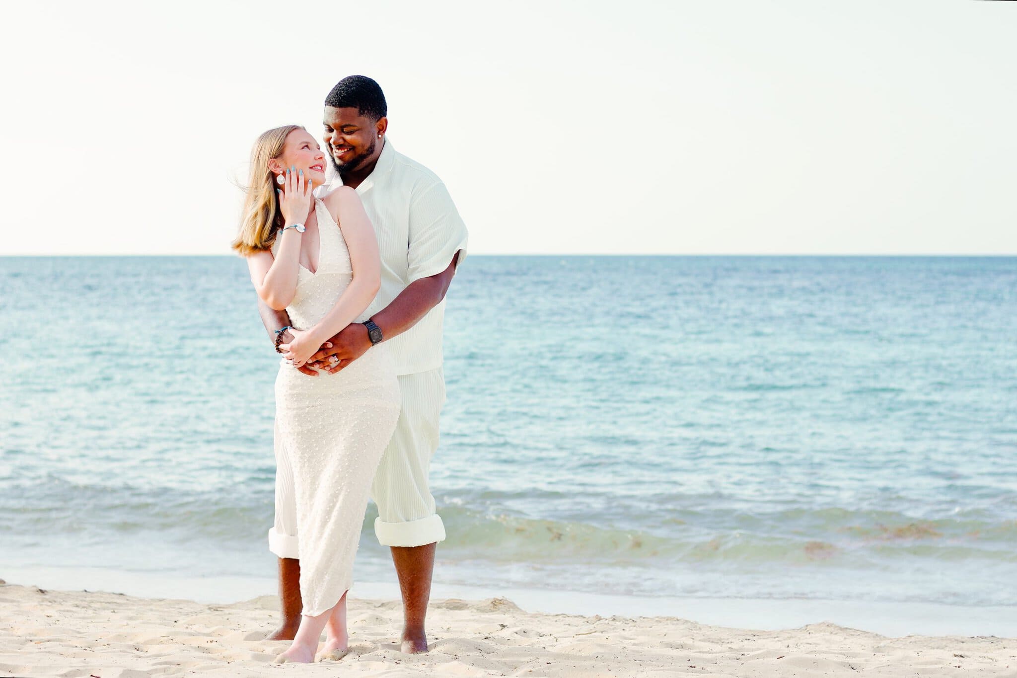 Couple smiling and embracing on the beach with the ocean behind them in Punta Cana