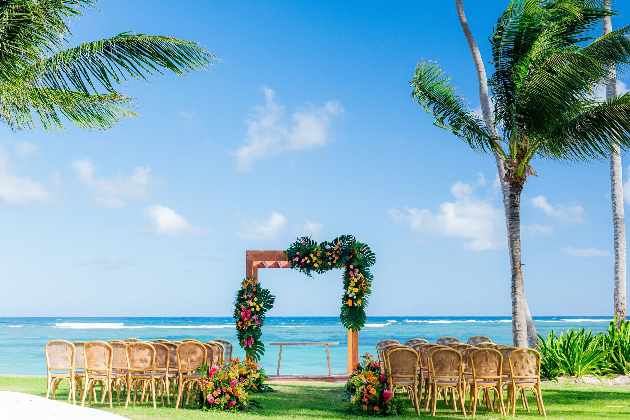 Oceanfront wedding ceremony setup in Punta Cana with a tropical floral arch, palm trees, and rows of chairs facing the sea