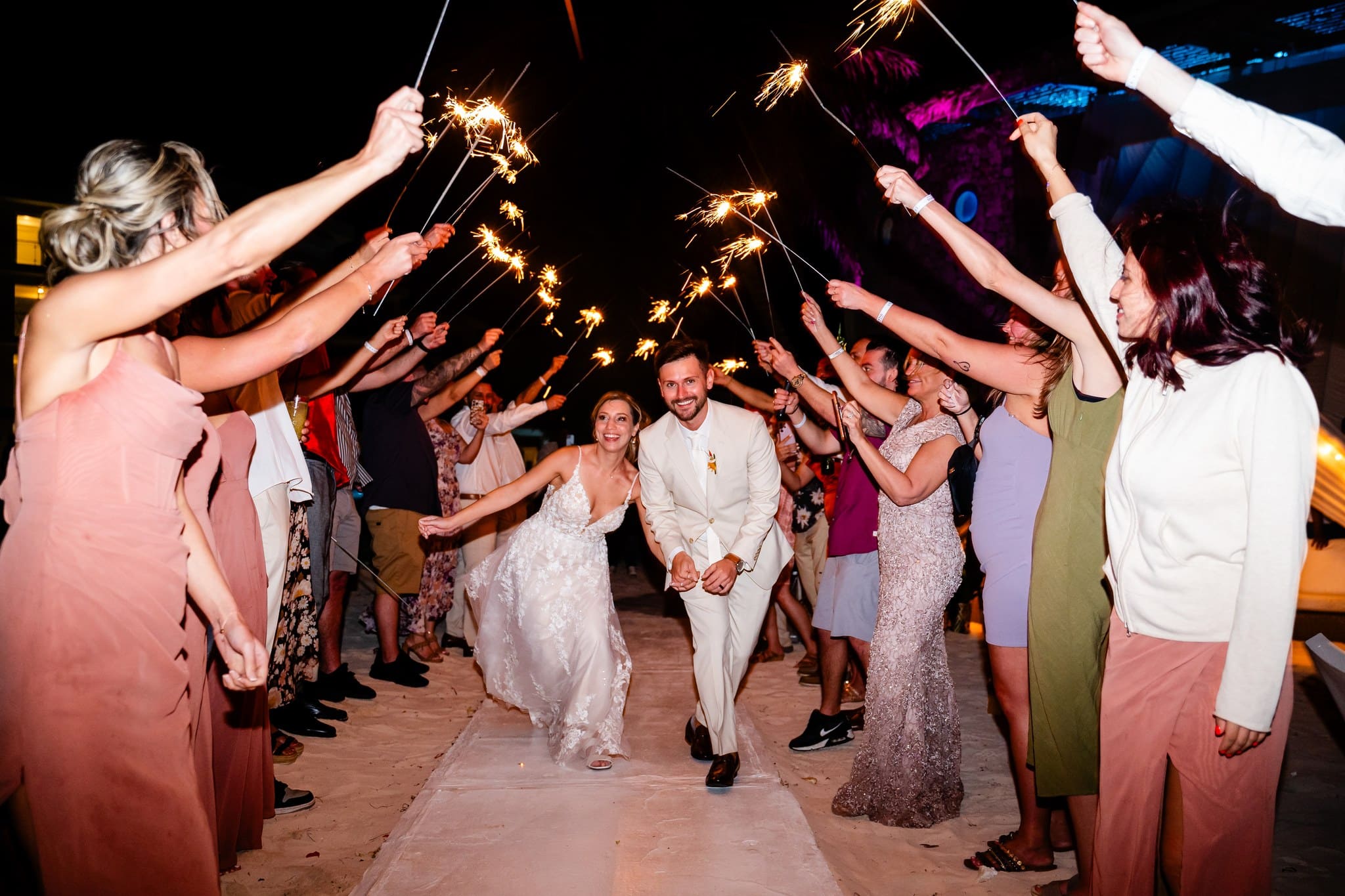 Newlyweds running hand in hand through a tunnel of sparklers held by their guests at a Punta Cana wedding