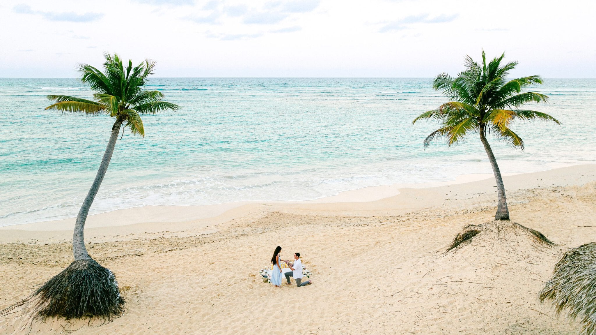 Marriage proposal on a wide sandy beach framed by two palm trees and turquoise ocean water in Uvero Alto