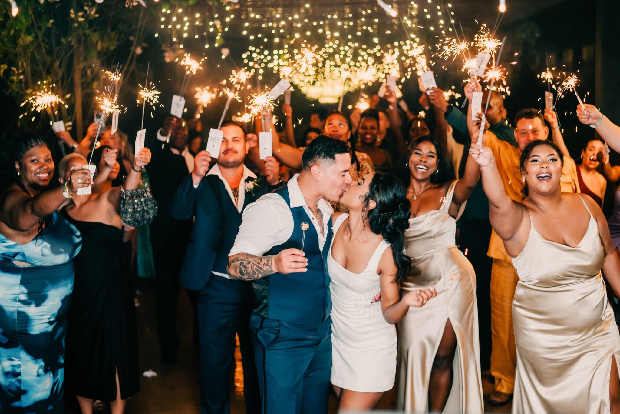 Newlyweds kissing during a sparkler exit as wedding guests celebrate around them